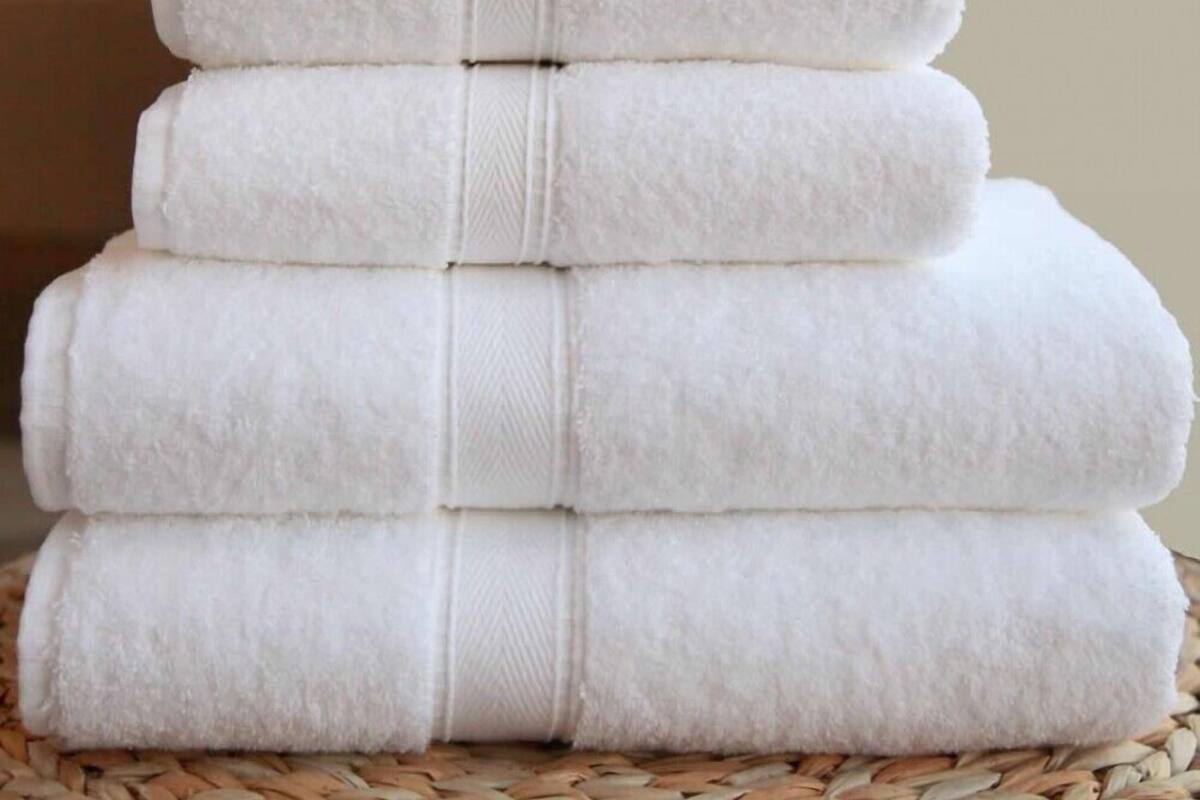 A stack of white towels arranged in a pyramid shape on a woven surface.