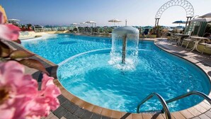 Una piscina con fuente de agua, tumbonas y sombrillas.