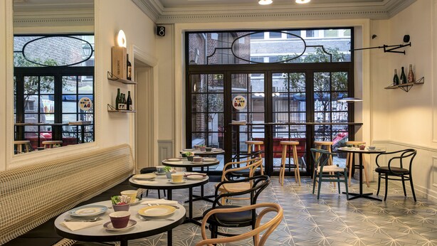 L’intérieur d’un restaurant avec des tables rondes, des chaises en osier et un sol à motifs.