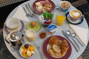 Une table de petit-déjeuner avec des croissants, du pain, des fruits, une tasse de café, un verre de jus et un pot de yaourt Danone.
