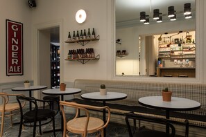 Un coin bar accueillant, avec des tables rondes et des chaises en osier, un banc carrelé et des étagères où sont exposées des bouteilles et des verres.