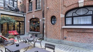 Un espace extérieur aménagé avec des tables et des chaises, un bâtiment en briques doté de grandes fenêtres et une porte avec un panneau de verre.
