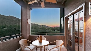 A balcony with wicker furniture, a table, and a view of a hilly landscape.