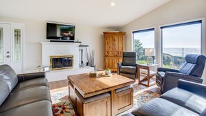 A spacious living room with a fireplace, leather sofas, a wooden coffee table, and a large window offering a view of the outdoors.
