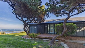 A modern house with a wooden deck, a small porch, and a view of the ocean.
