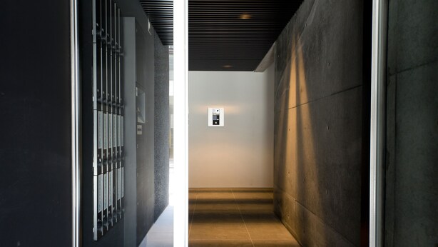 A narrow hallway with a modern design, featuring a glass partition on one side and a concrete wall on the other. A small, illuminated control panel is visible on the wall. - OH Inn -Fukuoka Stay- (Fukuoka)