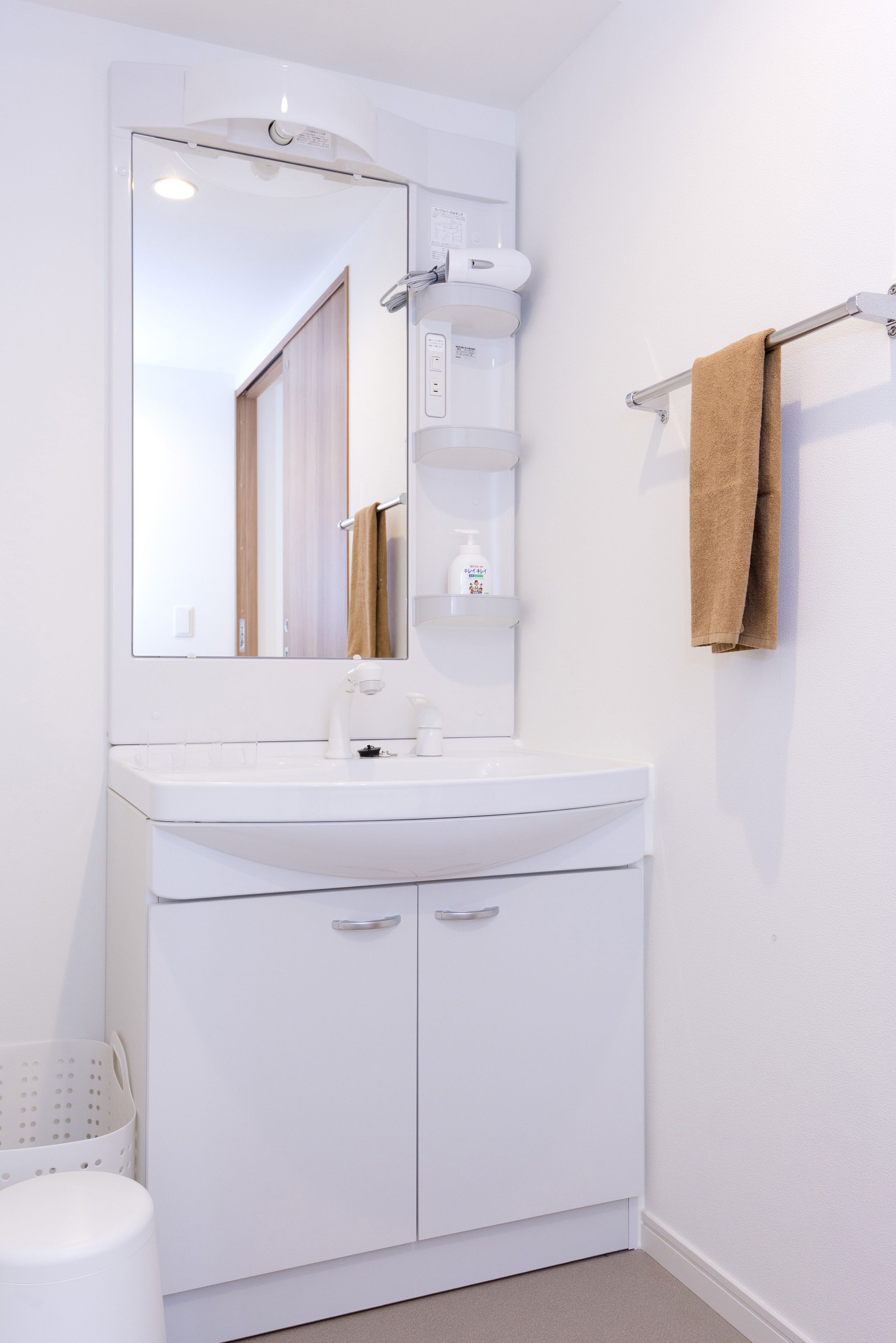 Un baño blanco con un espejo grande, un lavabo blanco, un perchero para toallas y un armario blanco.