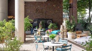 An outdoor seating area with tables and chairs, potted plants, and a brick wall with the name 'Ruby' in the background.