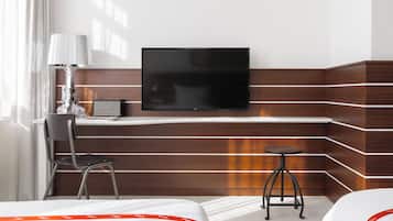 Une chambre d’hôtel comprenant un lit, un bureau avec une chaise, un téléviseur fixé au mur et un petit tabouret.