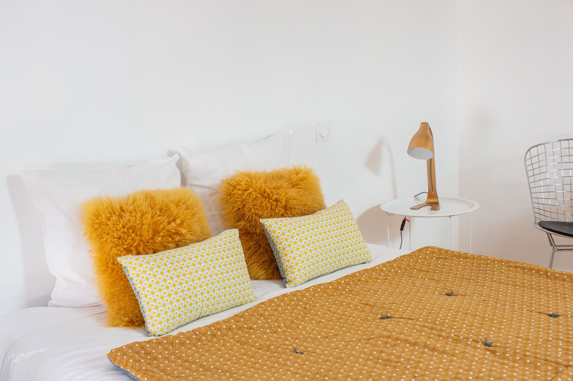A neatly made bed with a patterned bedspread and two pillows, one with a yellow and white pattern and the other with a solid yellow color.