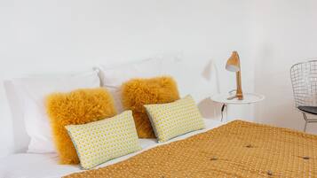 A neatly made bed with a patterned bedspread and two pillows, one with a yellow and white pattern and the other with a solid yellow color.