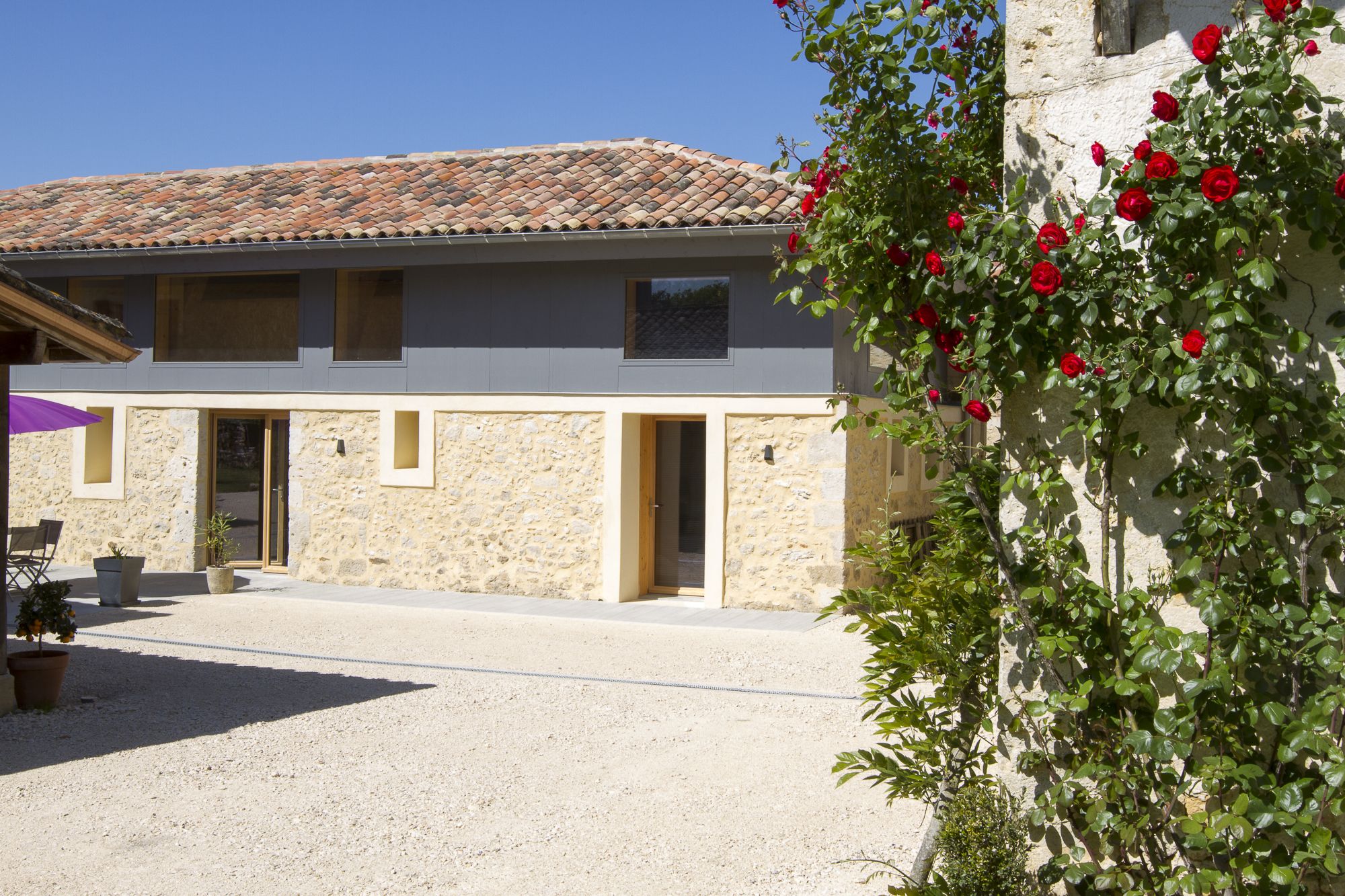 A building with a stone facade, a tiled roof, and a gravel courtyard.