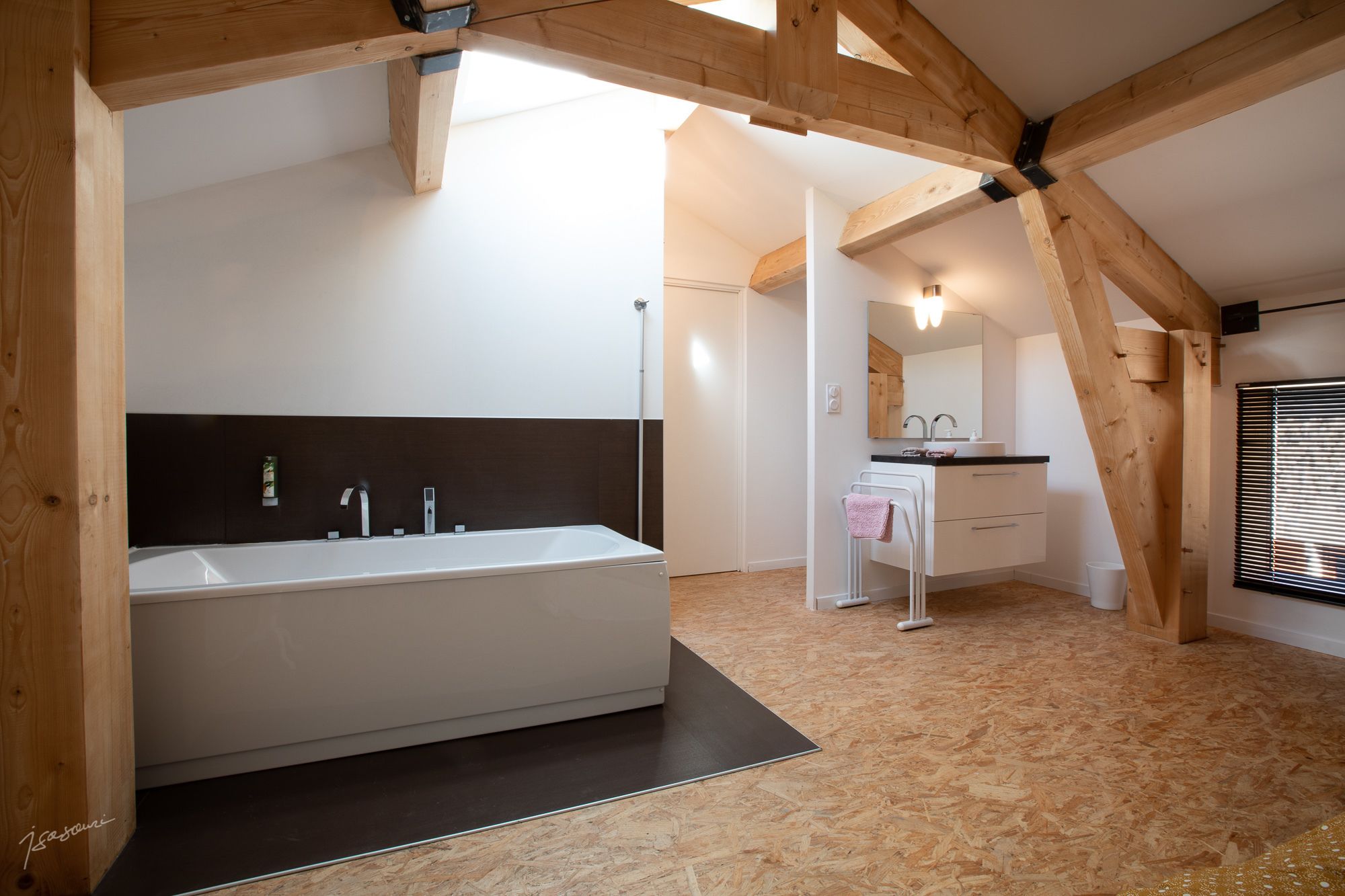 A modern bathroom with a large bathtub, a separate sink area, and a wooden ceiling structure.