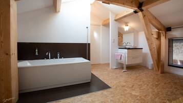 A modern bathroom with a large bathtub, a separate sink area, and a wooden ceiling structure.