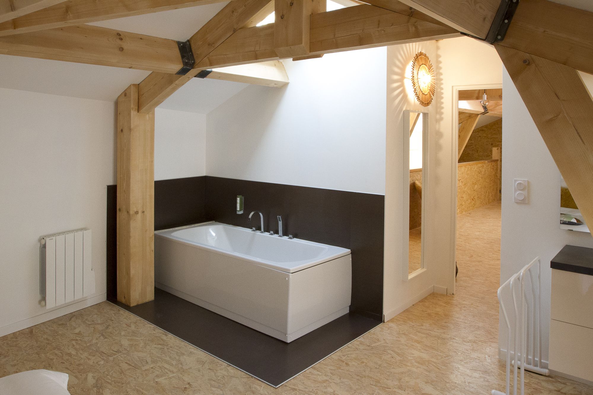 A modern bathroom with a freestanding bathtub, wooden beams, and a sloped ceiling.