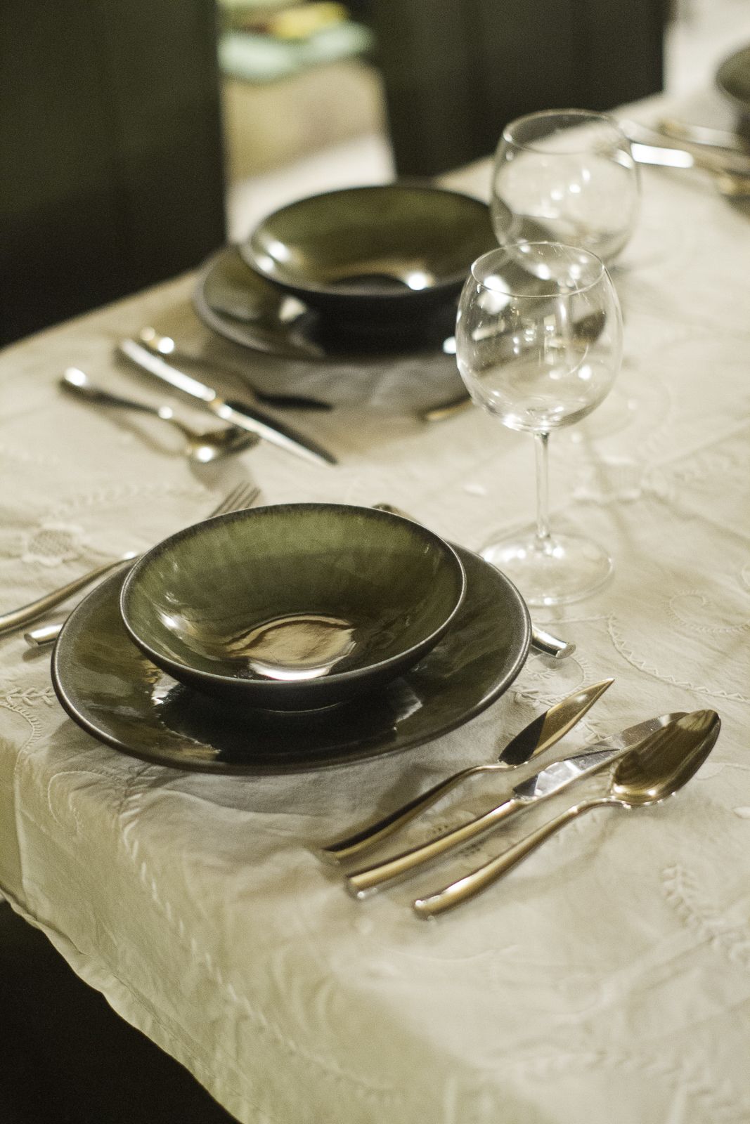 Una mesa dispuesta con platos negros, cubiertos y copas de vino, cubierta por un mantel blanco.