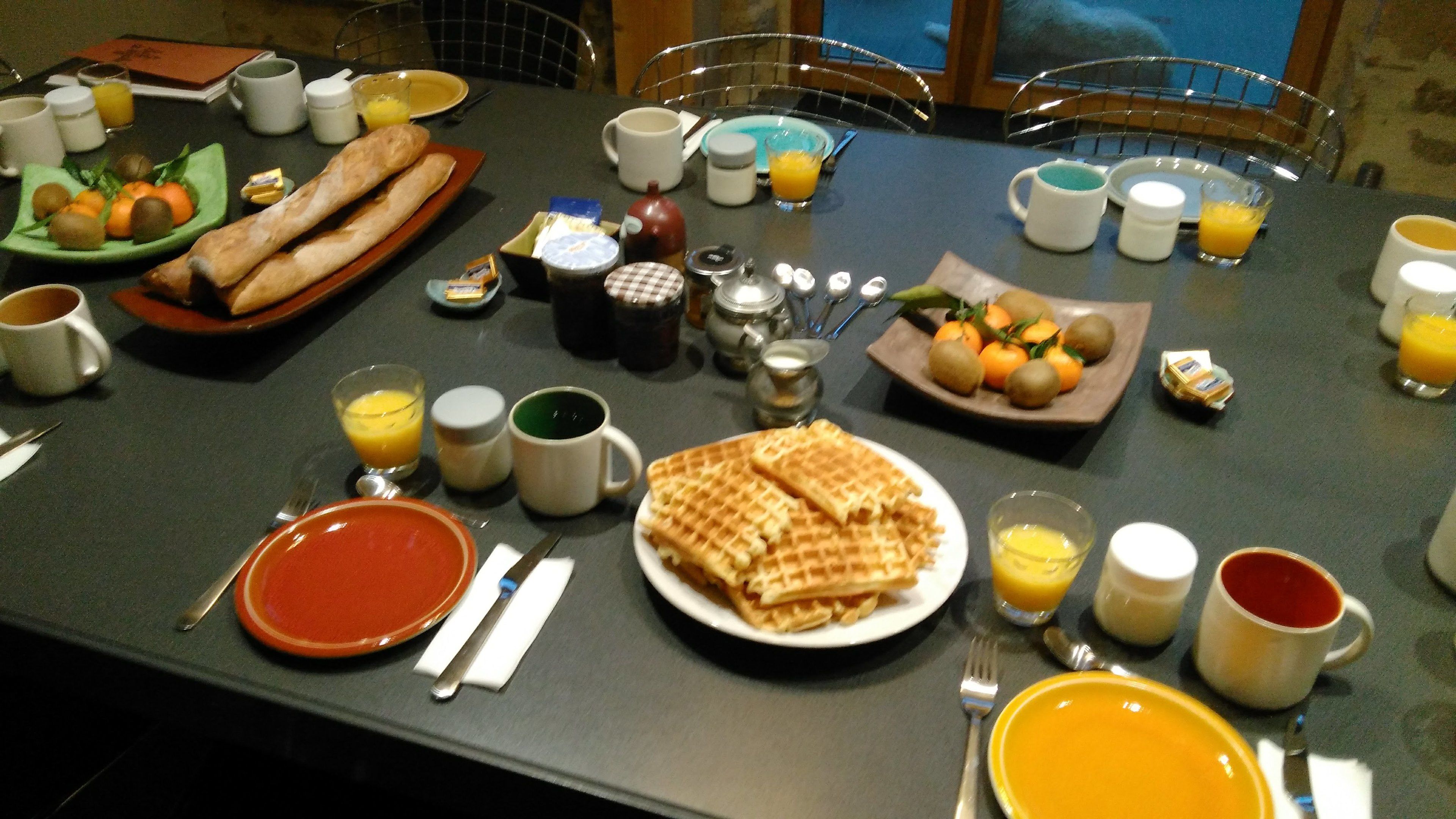 A breakfast table set with plates of waffles, toast, and fruit, along with various condiments and beverages.