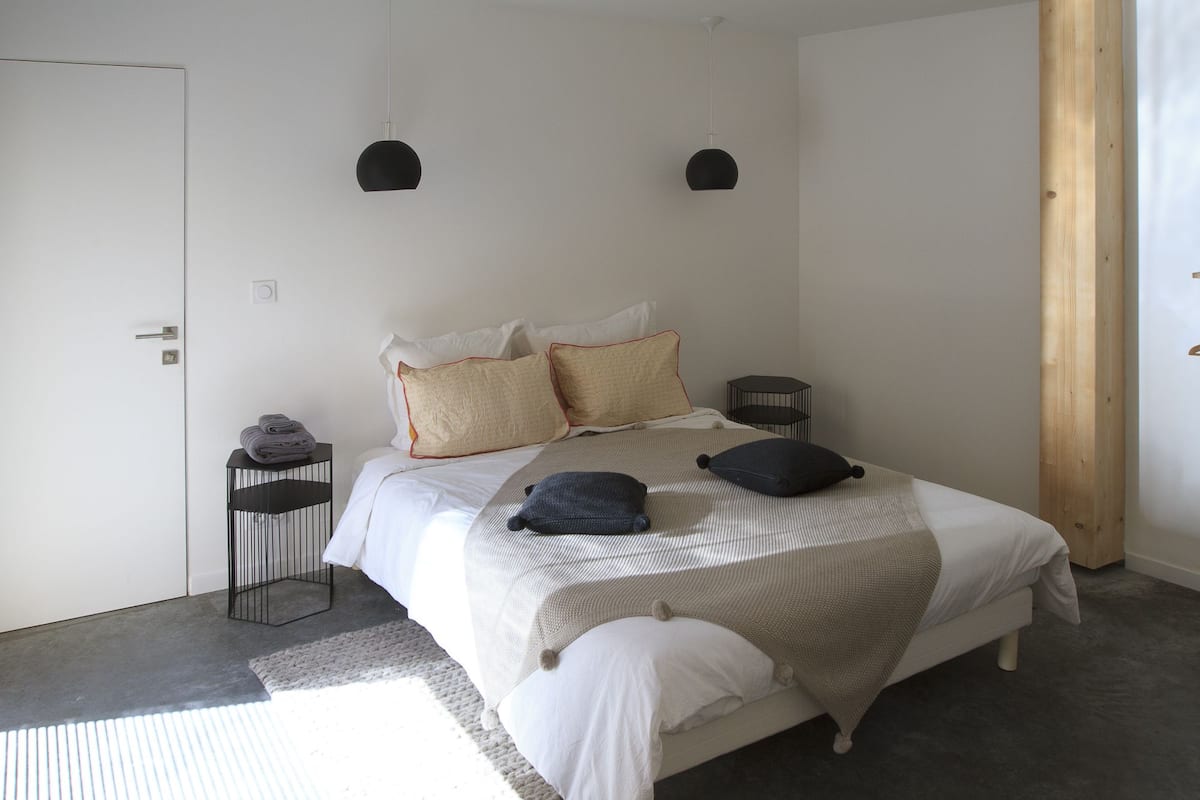 A bedroom with a bed, pillows, a bedside table, and a hanging light fixture.