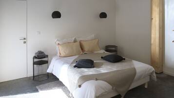 A bedroom with a bed, pillows, a bedside table, and a hanging light fixture.