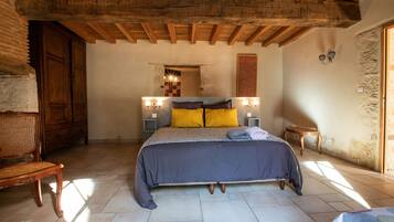 A bedroom with a bed, wooden headboard, two wall-mounted light fixtures, a wooden chair, and a small table.
