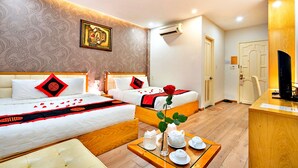 A hotel room with two beds, a wooden desk, a vase with a rose, and a tray with teacups and a pitcher. - HANZ MinhVy Hotel (Ho Chi Minh City)