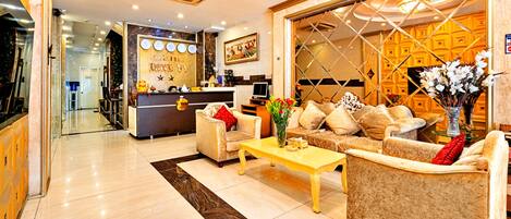 A hotel lobby with a reception desk, seating area, and a large window with a geometric pattern.