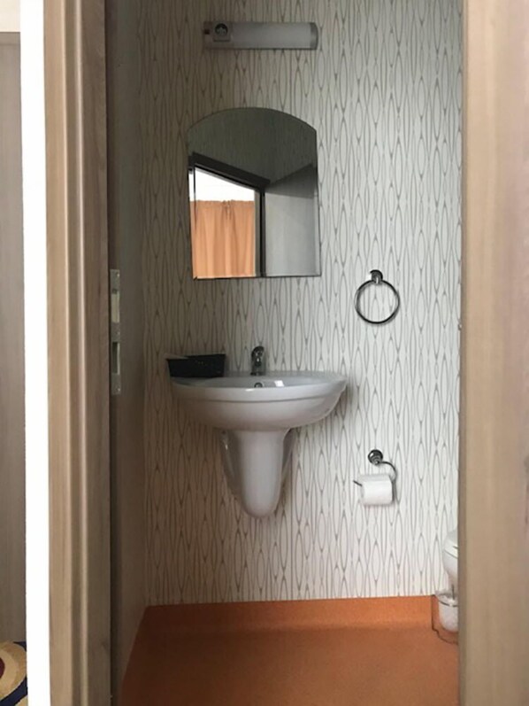 A bathroom with a sink, mirror, towel ring, and toilet paper holder.