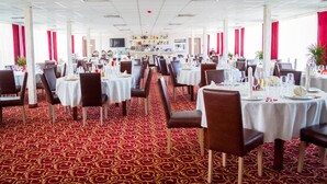A formal dining area with round tables, white tablecloths, and red patterned carpet.