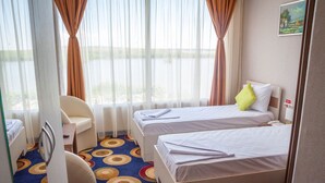 A hotel room with two beds, a desk, a chair, and a view of the outdoors.