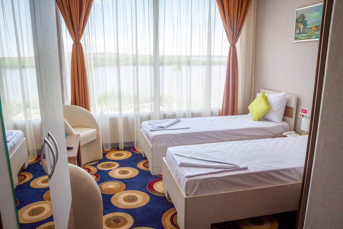 A hotel room with two beds, a desk, a chair, and a view of the outdoors.