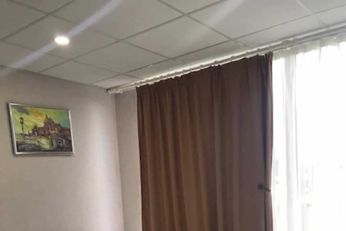 A hotel room with a bed, pillows, a painting on the wall, and a window with curtains.