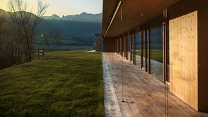 A modern building with a wooden deck and large windows offering a view of a mountain range. - Casariga (Comano Terme)