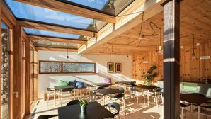 A modern interior with wooden walls and a skylight, featuring a dining area with tables and chairs, a kitchen area, and a stone wall. - Casariga (Comano Terme)