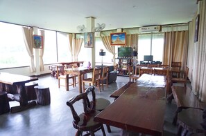 A spacious room with multiple wooden tables and chairs, a television, and a ceiling fan.