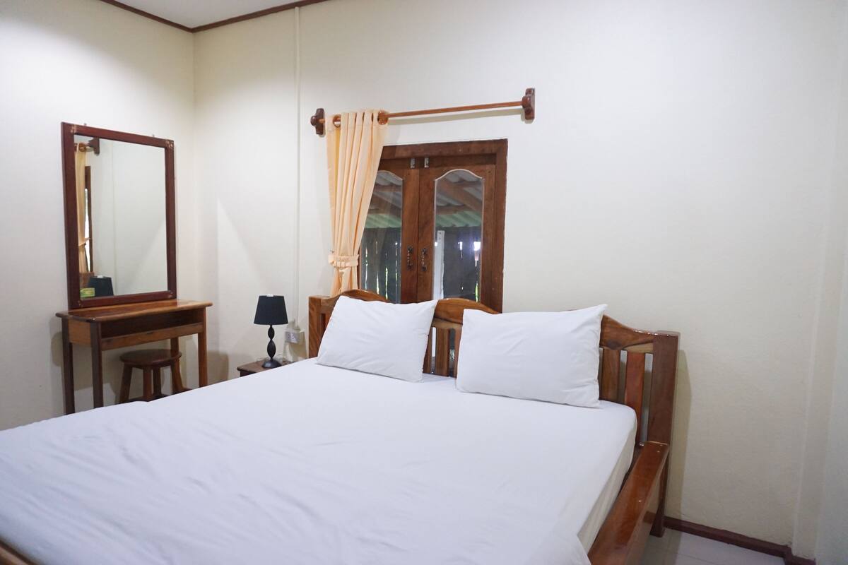 A neatly made bed with white linens, a wooden headboard, and a bedside table with a lamp.