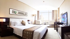 A hotel room with a large bed, a TV, a desk, and a view of the city. - Elegance Hotel Tianjin (Tianjin)