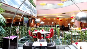 A modern indoor dining area with glass tables and red chairs, surrounded by greenery and decorative elements. - Elegance Hotel Tianjin (Tianjin)