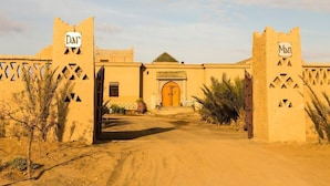 A desert-style building with a large wooden door, two towers with signage, and a clear sky. - Dar Mari (Taouz)