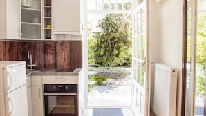 Una cocina compacta con armarios blancos, horno integrado y vistas a un jardín a través de un ventanal.