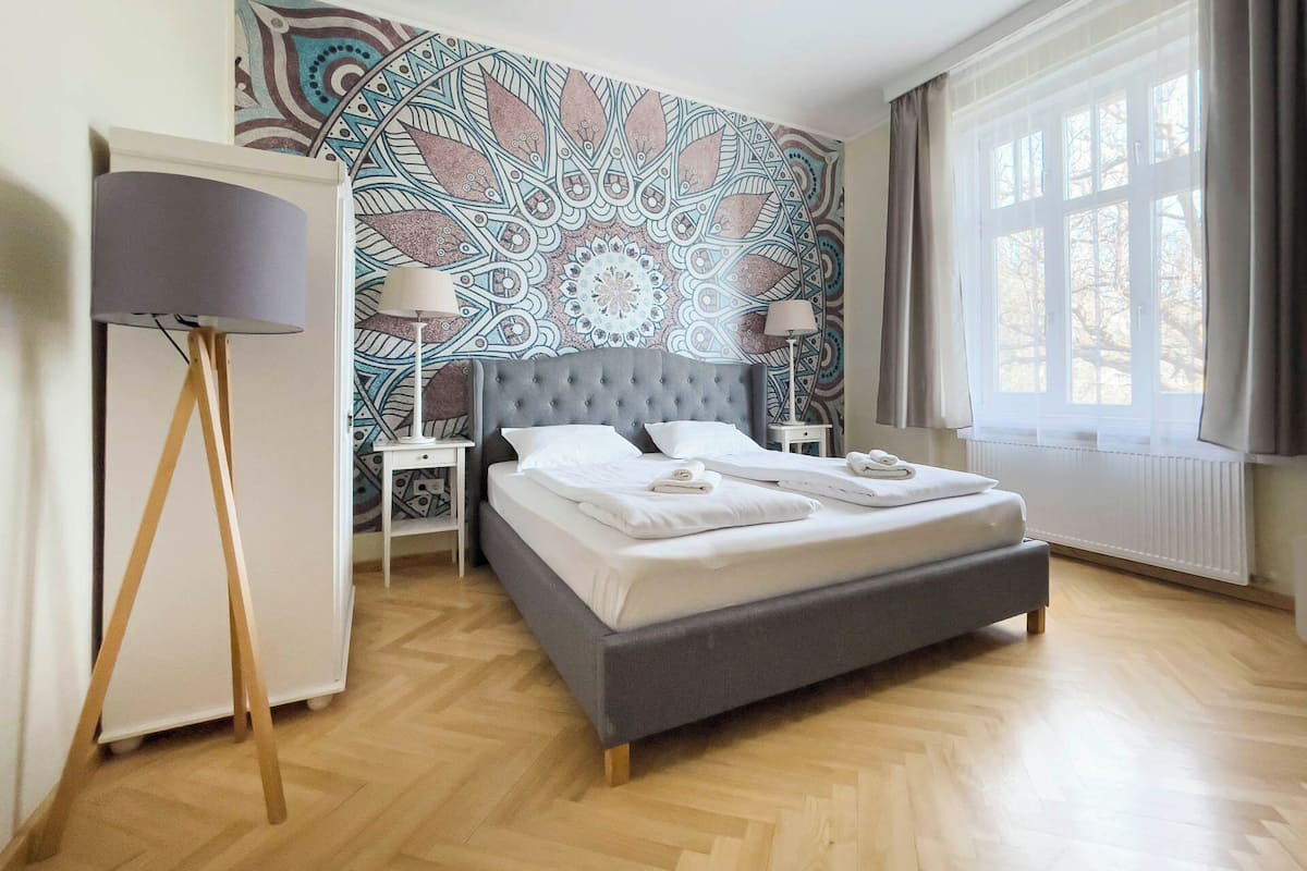 Une chambre avec un grand lit, deux tables de chevet, une lampe sur pied et un mur décoré d’un motif.