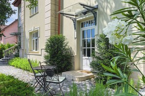 A building with a stone facade, a door with glass panels, and a small outdoor seating area with a table and chairs. - Villa Fontana (Balatonfured)