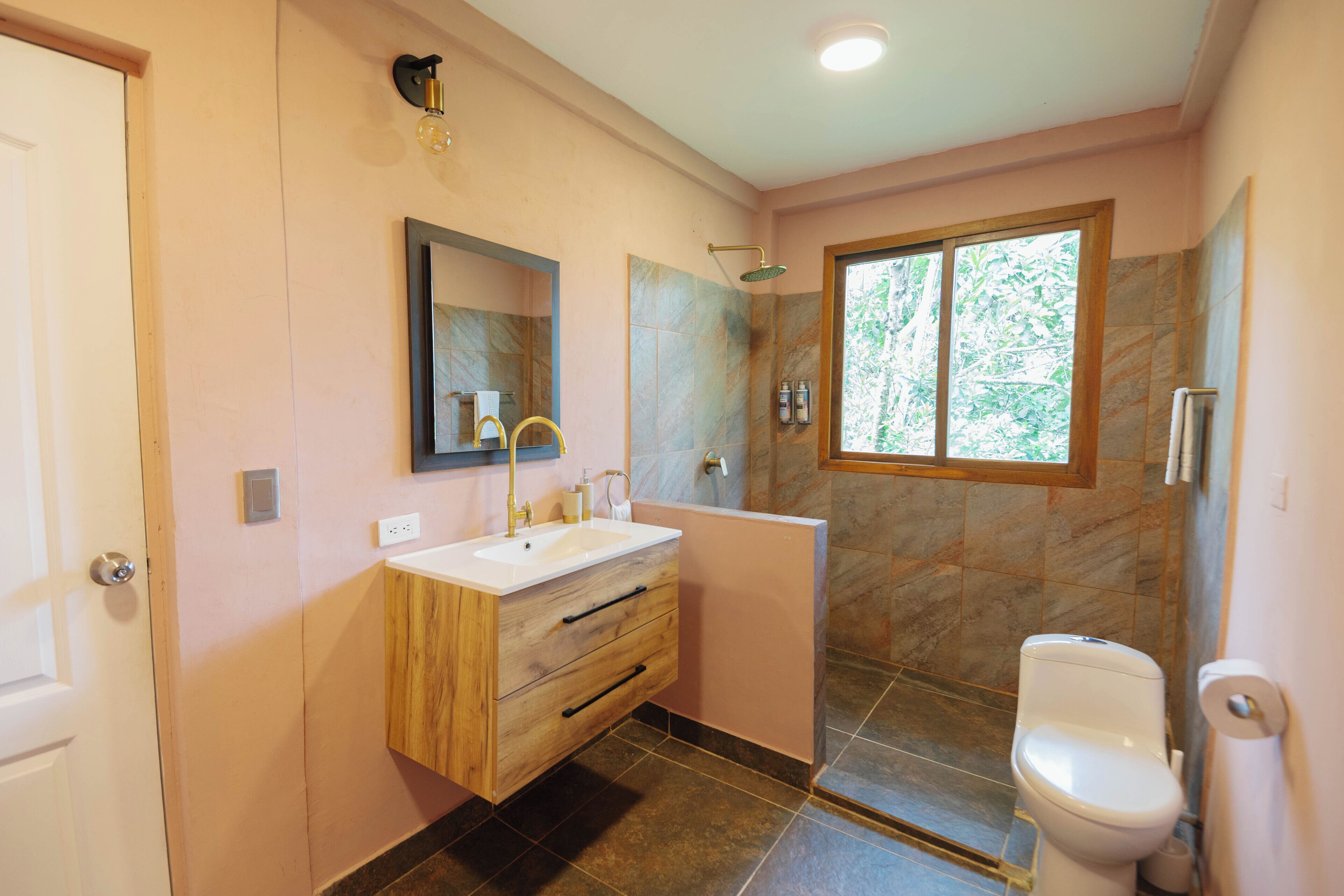 Un baño con tocador de madera, lavabo, espejo, ducha e inodoro.