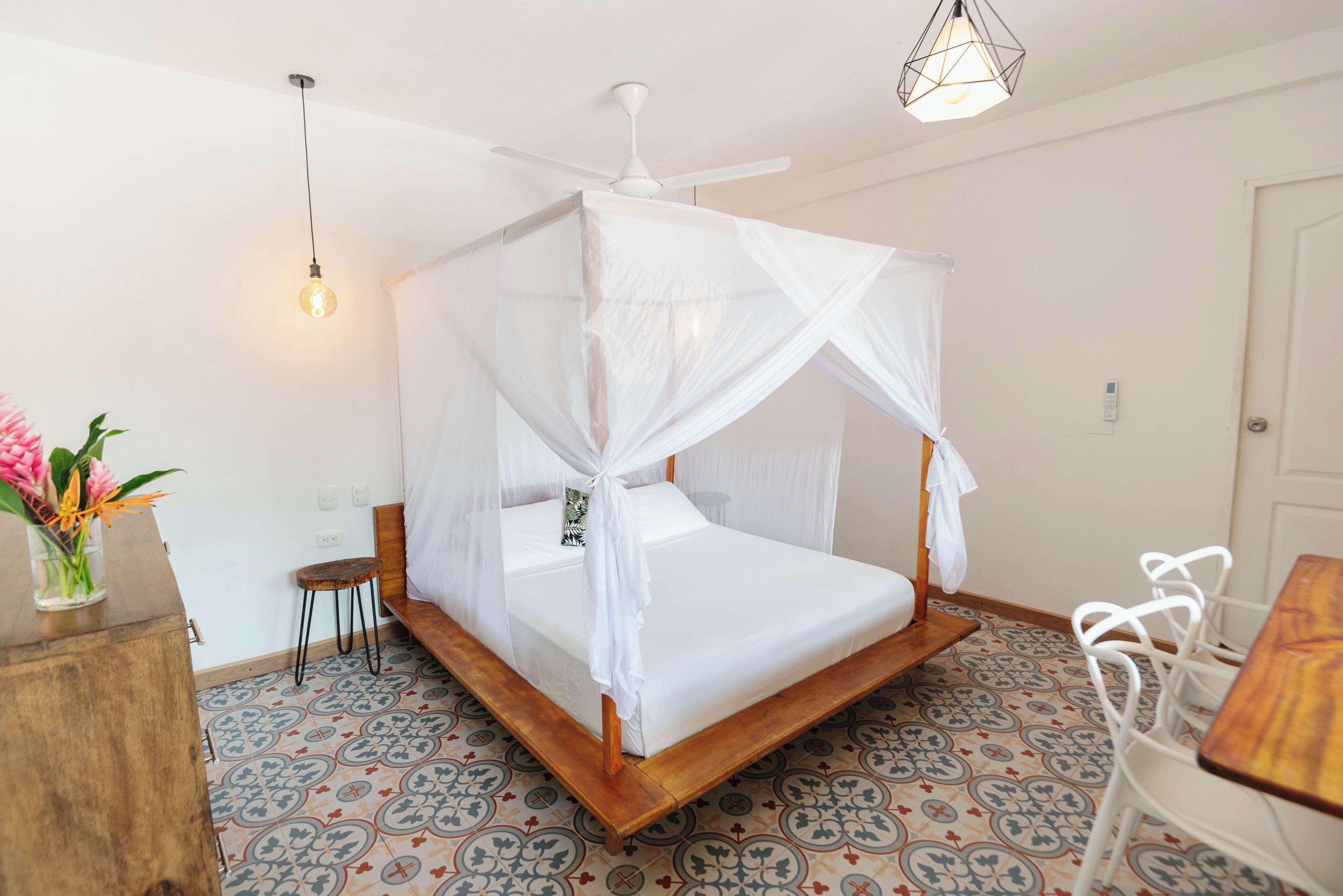Una stanza con un letto a baldacchino, una ventola a soffitto, un tavolo e una sedia.