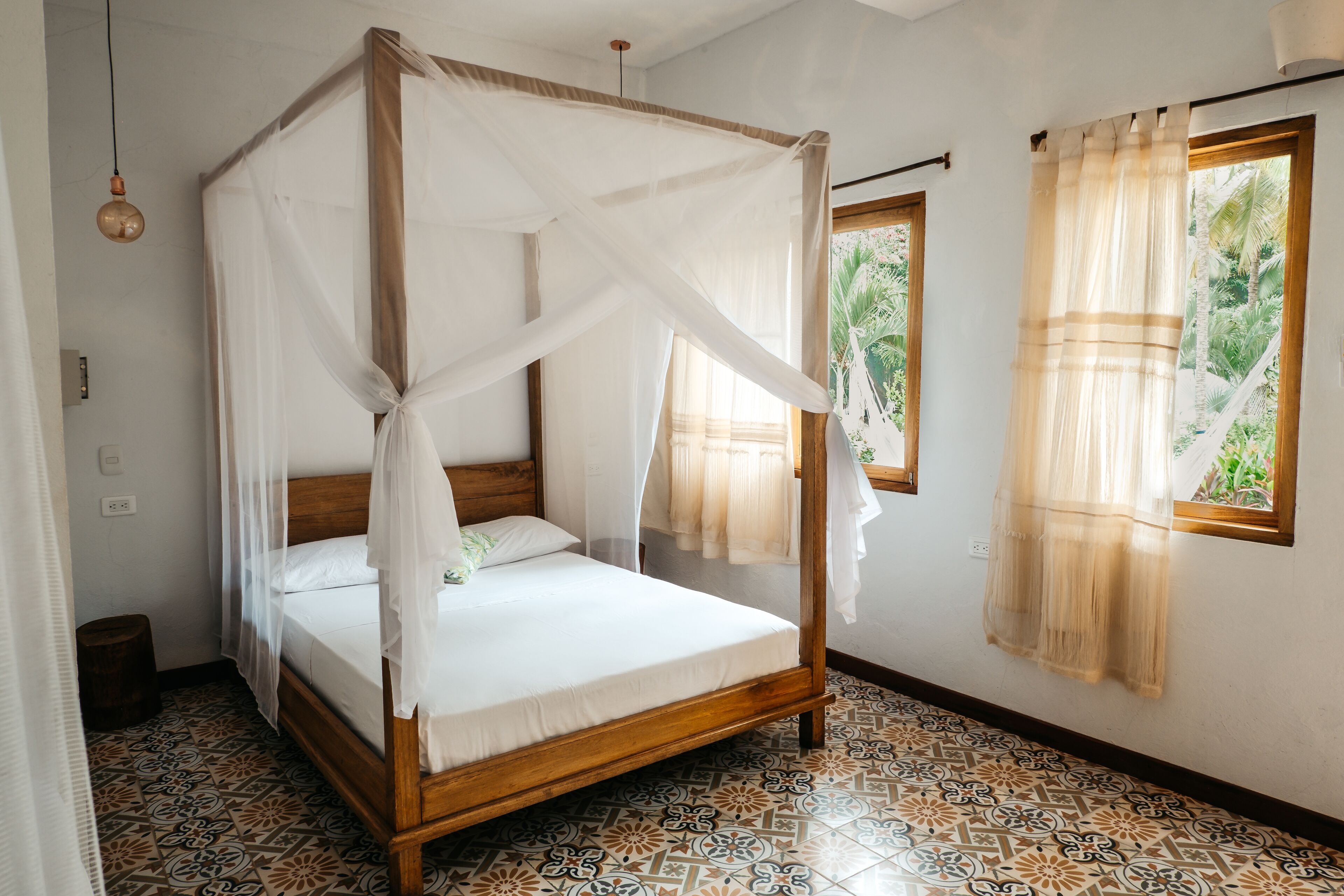 Una cama con dosel de madera y ropa blanca, un suelo estampado y una ventana con cortinas.