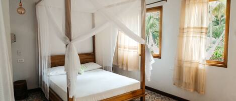 Una cama con dosel de madera y ropa blanca, un suelo estampado y una ventana con cortinas.