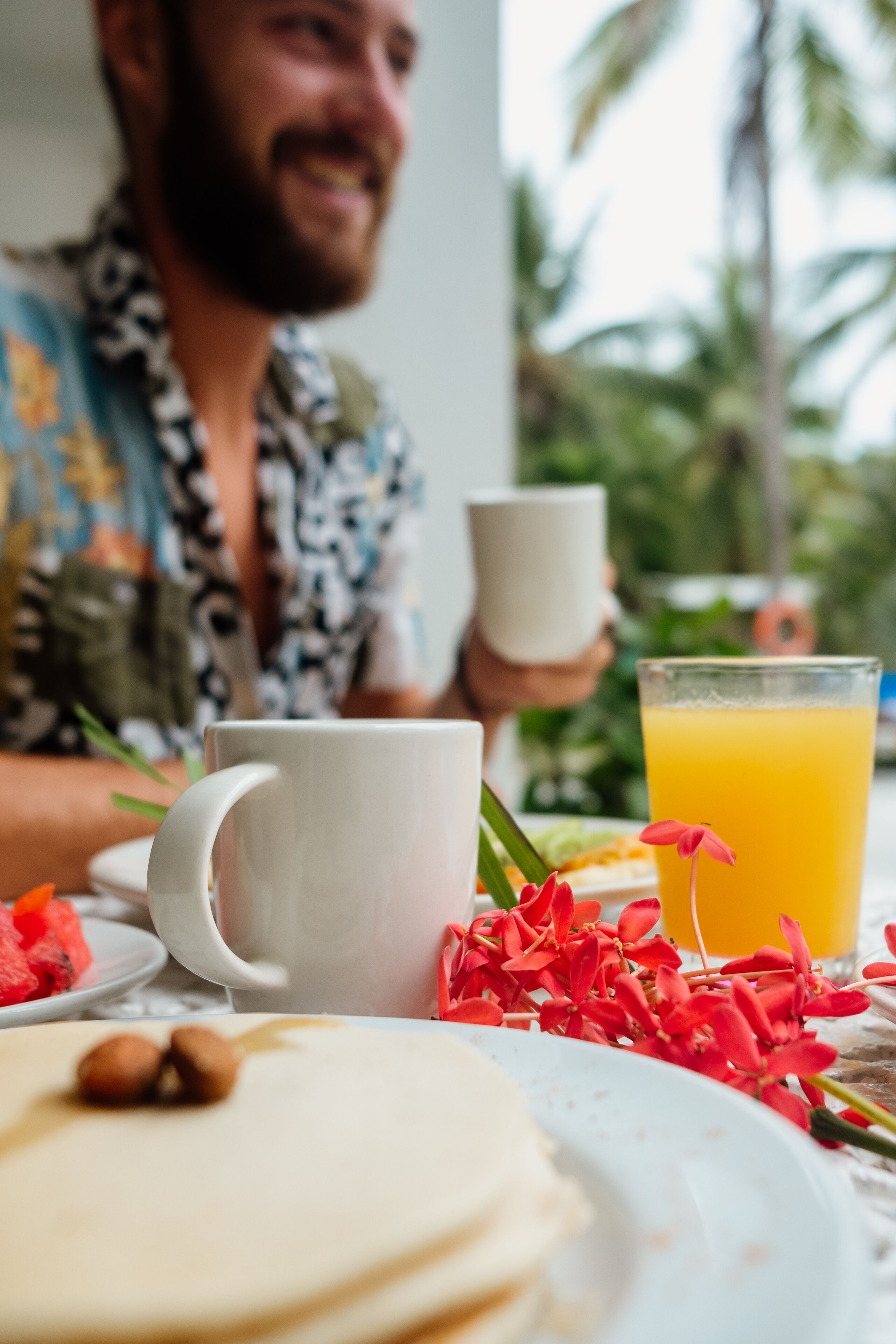 Un desayuno con una taza blanca, un vaso de zumo de naranja y un plato con comida y flores.