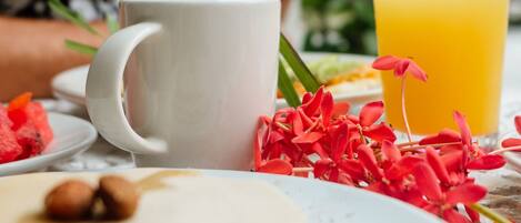 Un desayuno con una taza blanca, un vaso de zumo de naranja y un plato con comida y flores.