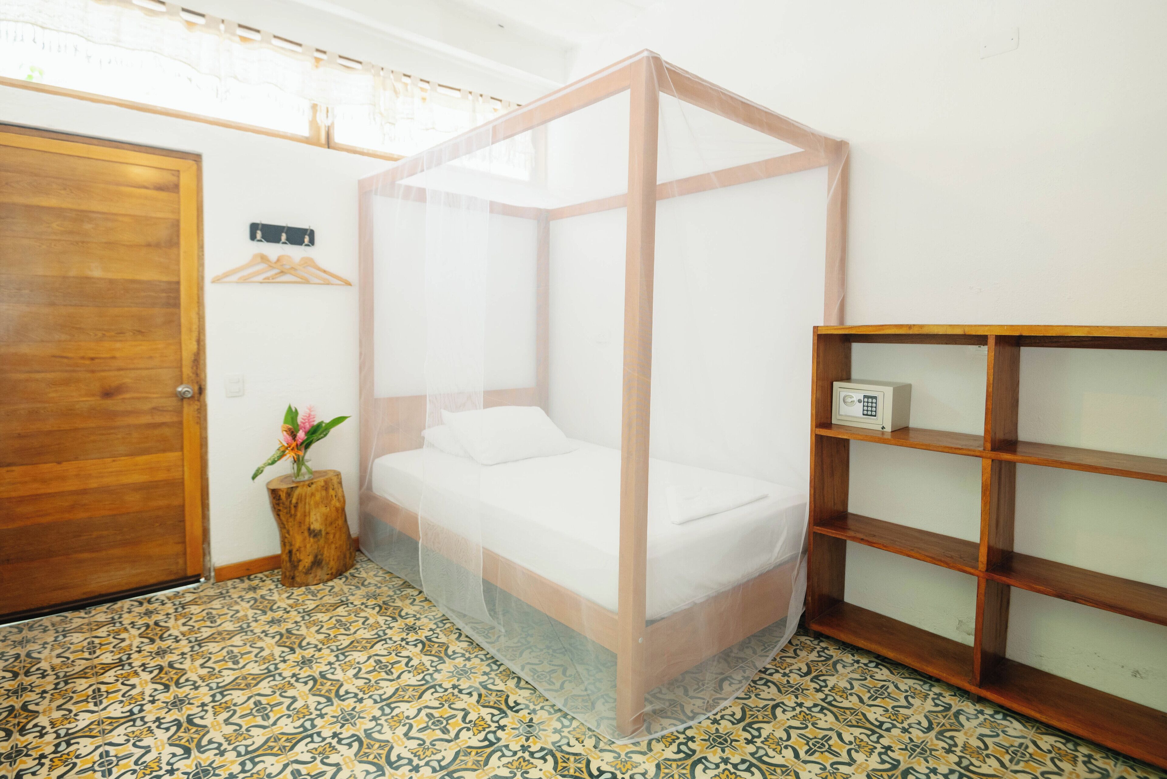 Una habitación con una cama con dosel, una puerta de madera, un taburete pequeño de madera con una planta y una estantería.