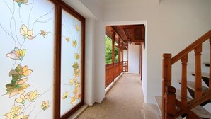 A hallway with a wooden staircase, a decorative wall with floral patterns, and a view of an outdoor wooden deck. - Deger Apart (Ula)