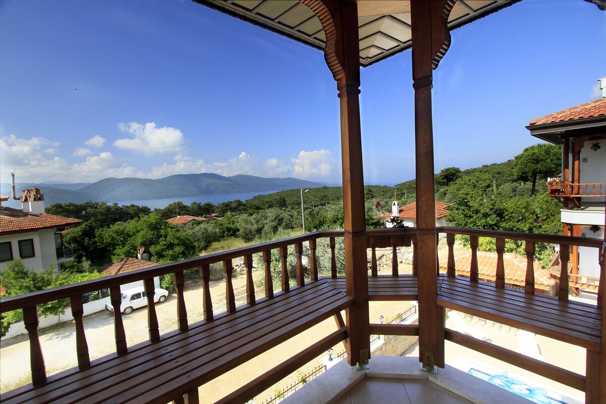 A wooden balcony with a view of a mountainous landscape and a body of water.